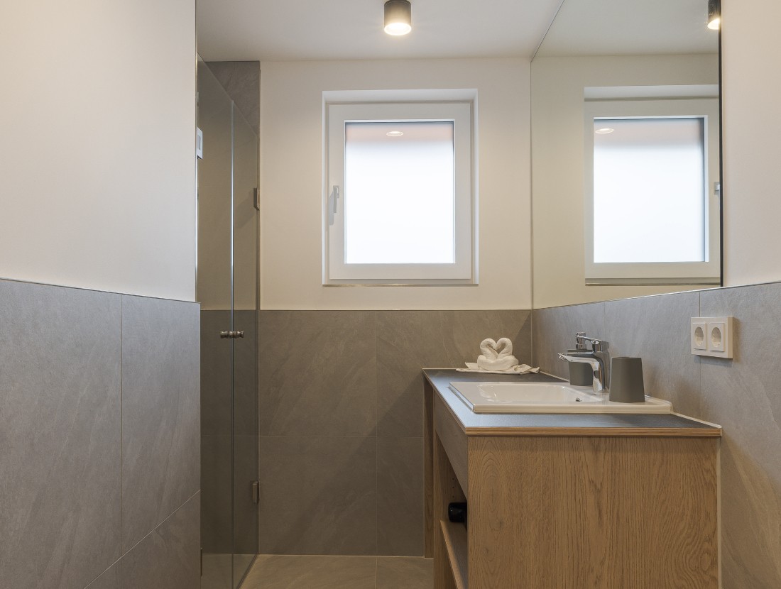 Modernes Bad mit Dusche, Waschbecken und gro&szlig;em Spiegel unter einem Fenster