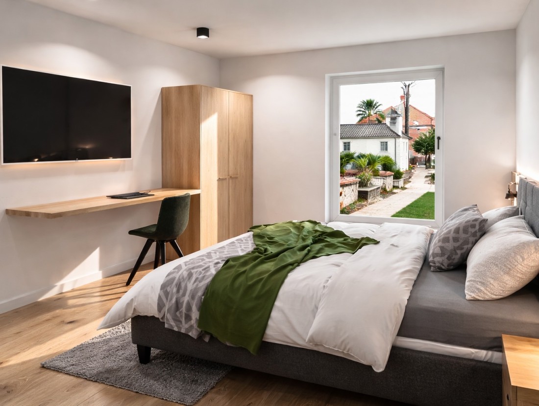 Modernes Schlafzimmer mit Bett, Schreibtisch, Fernseher und Blick auf einen Garten
